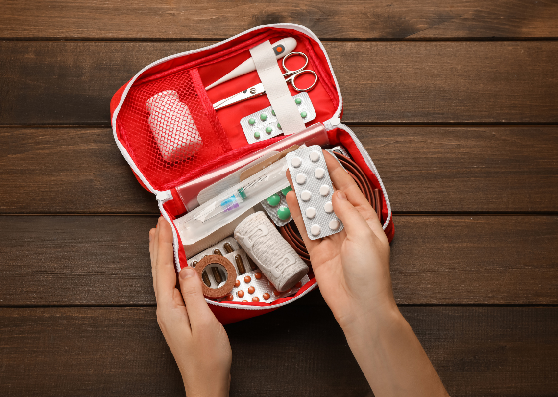 Hands holding a first aid kit with medicine and medical supplies.
