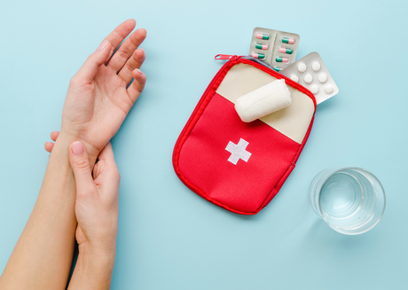  Hand close to red first aid kit with water and pills