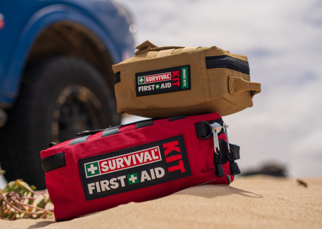 Two survival first aid kits on sandy ground.