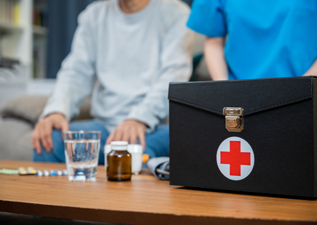 Black medical kit with red cross, pills, and medicine bottle on table