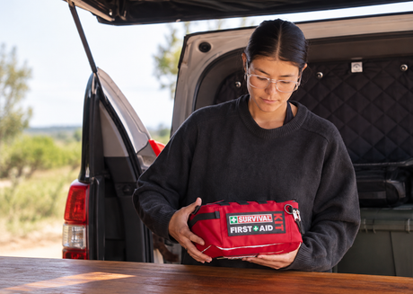 Person holding red SURVIVAL first aid kit outdoors