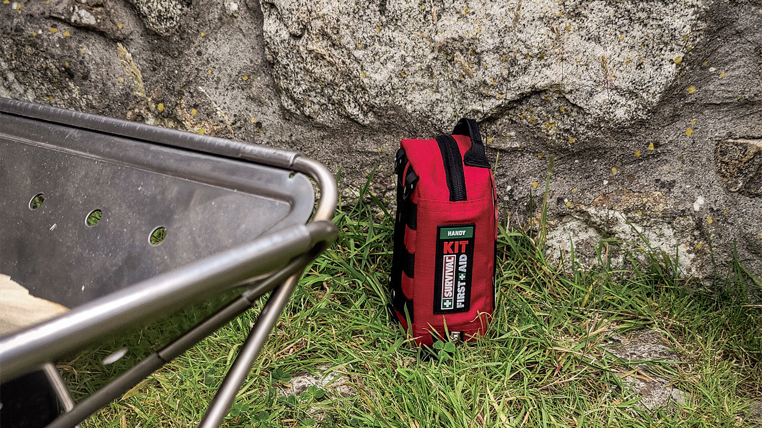 Red first aid kit on grass by a stone wall